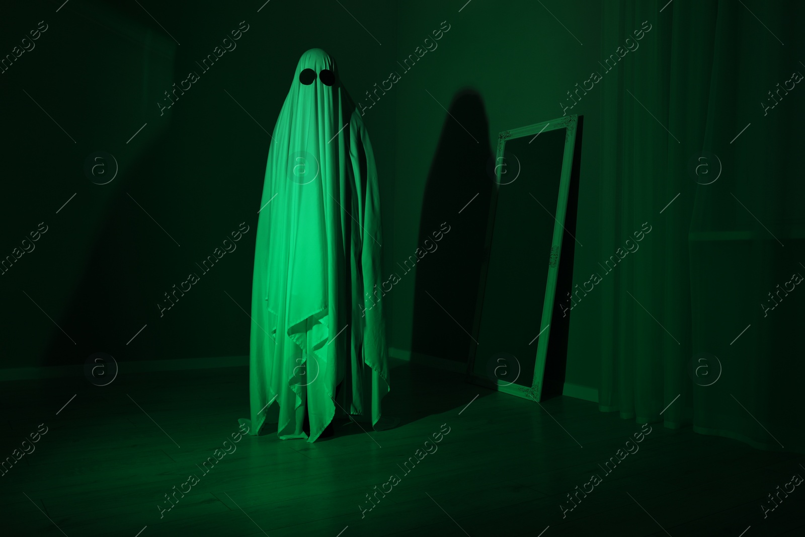 Photo of Creepy ghost. Woman covered with sheet in green light