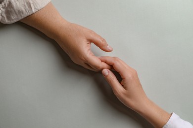 Woman holding hands with her mother light grey background, top view