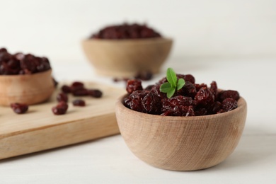 Photo of Tasty dried cranberries and leaves in bowl on white table. Space for text