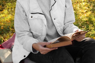 Woman reading book in park on autumn day, closeup