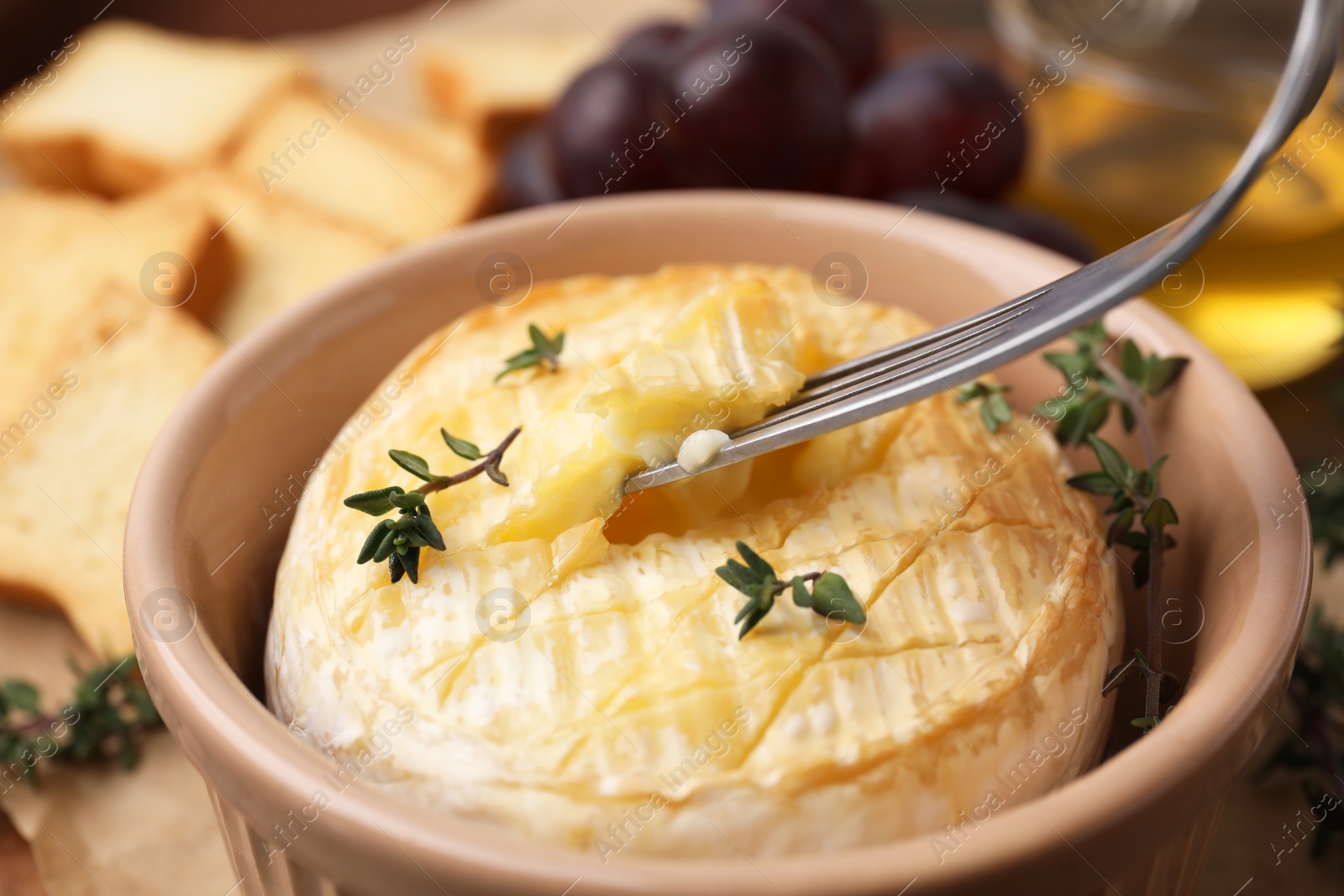 Photo of Taking tasty baked camembert with fork from bowl on table, closeup