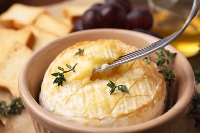 Photo of Taking tasty baked camembert with fork from bowl on table, closeup
