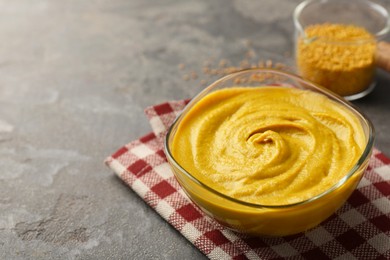 Tasty mustard sauce in glass bowl on grey textured table, space for text