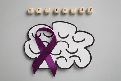 Word Epilepsy made of wooden cubes with letters, paper brain cutout and purple ribbon on light grey background, flat lay