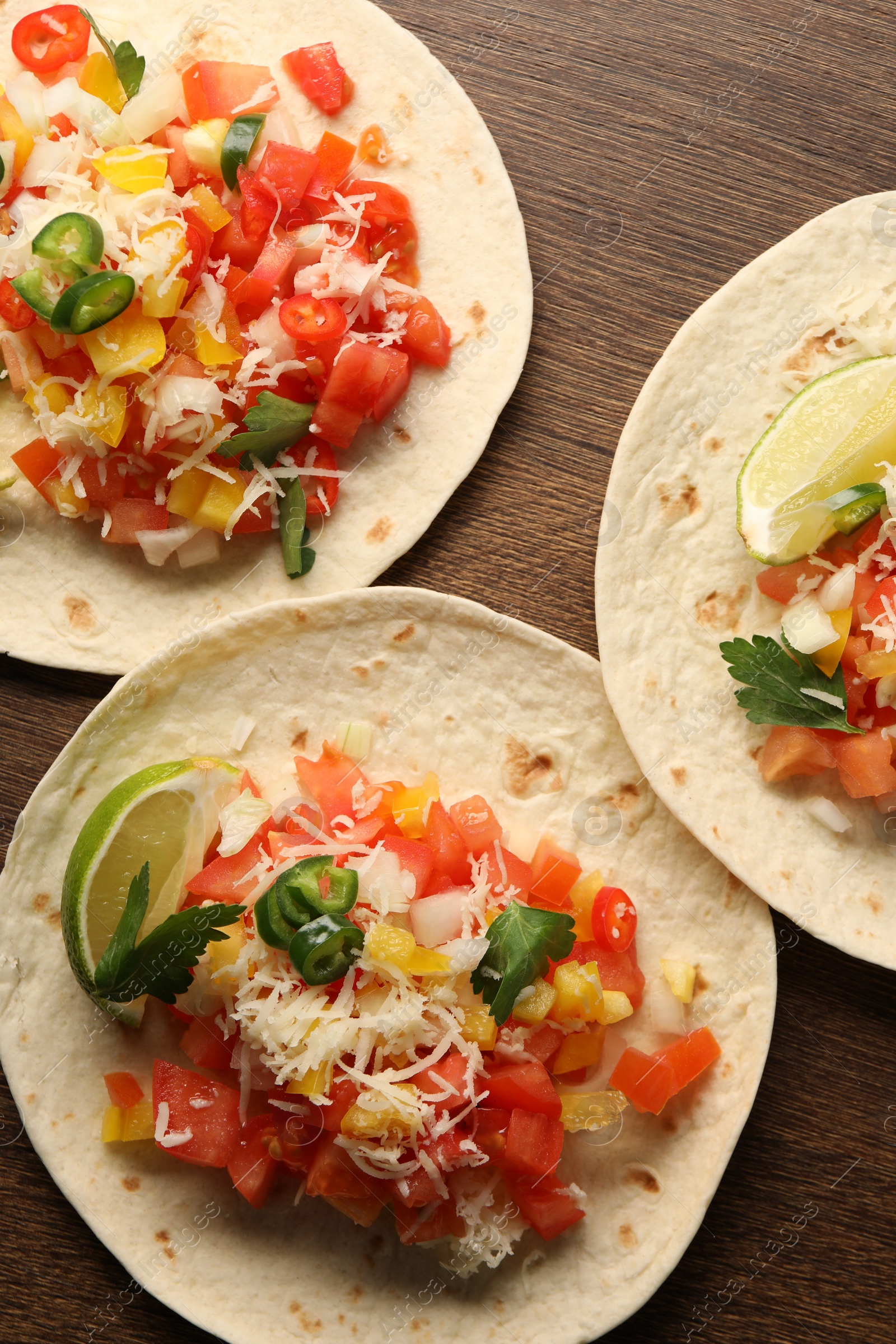 Photo of Delicious tacos with vegetables and lime on wooden table, top view