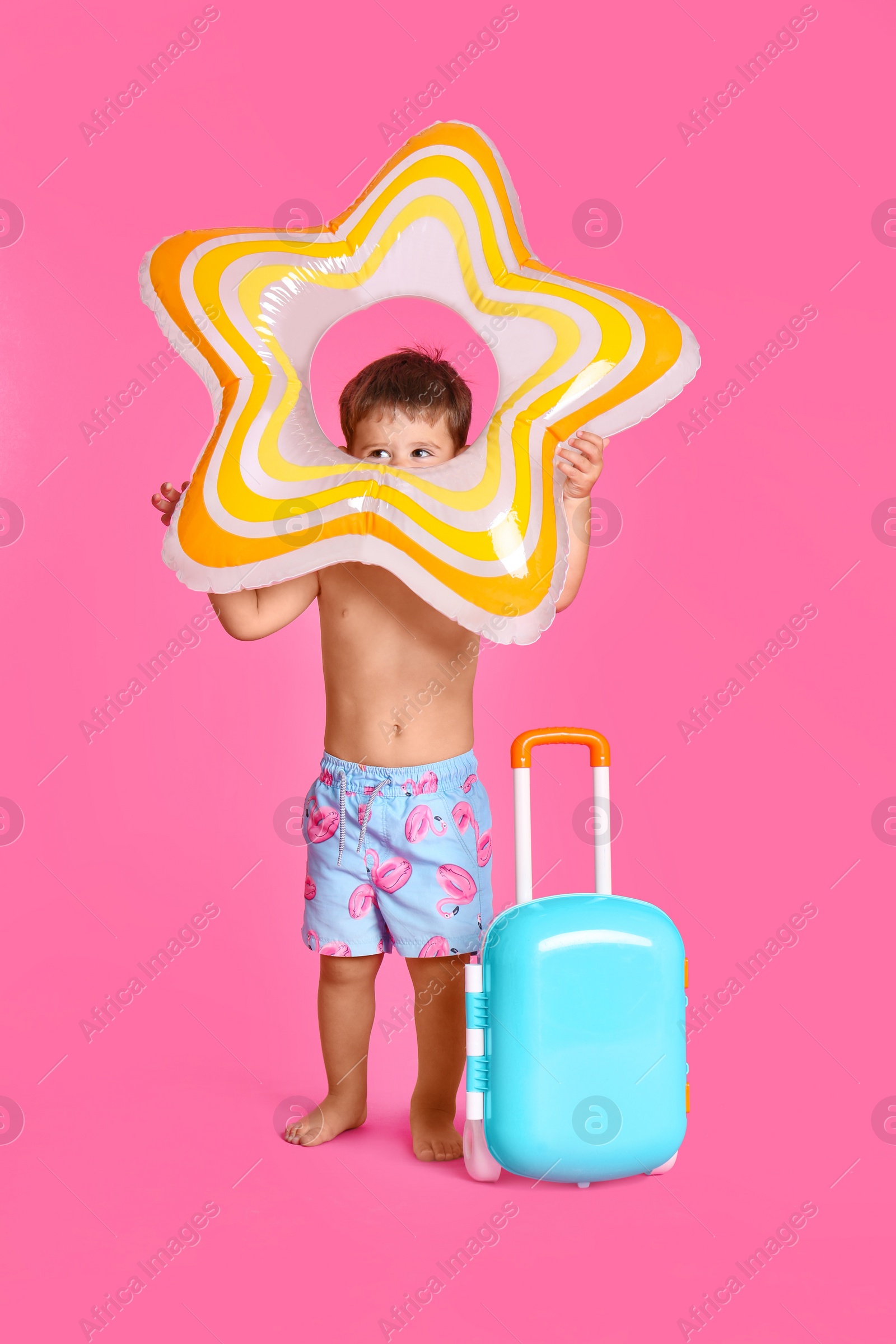 Photo of Cute little boy with inflatable ring and blue suitcase on pink background