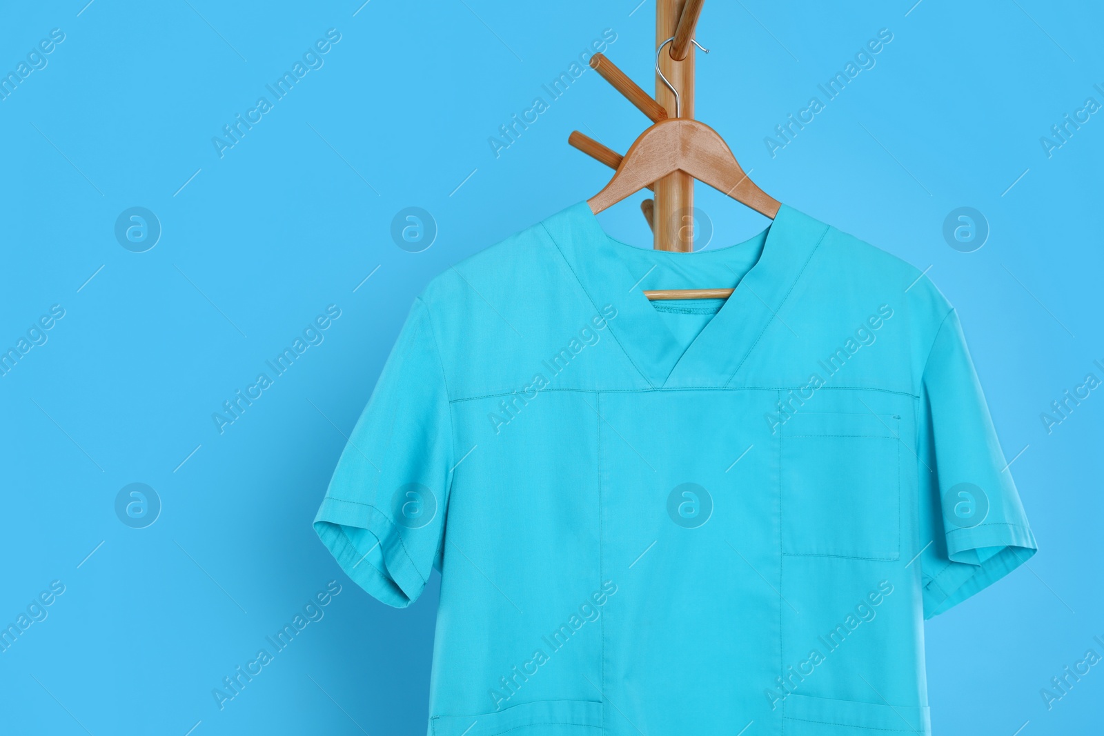 Photo of Turquoise medical uniform hanging on rack against light blue background. Space for text