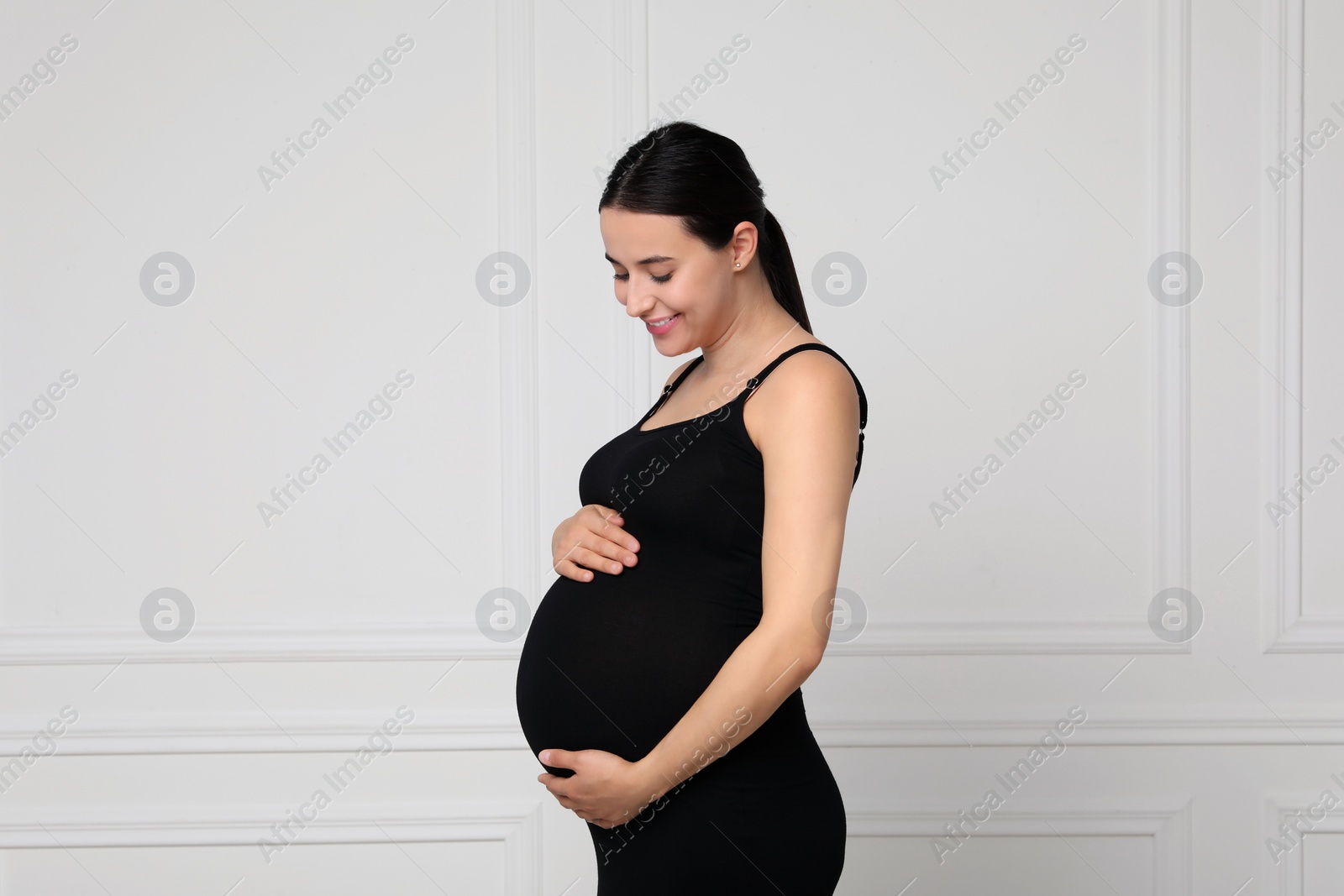 Photo of Beautiful pregnant woman in black dress near light grey wall