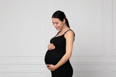 Beautiful pregnant woman in black dress near light grey wall