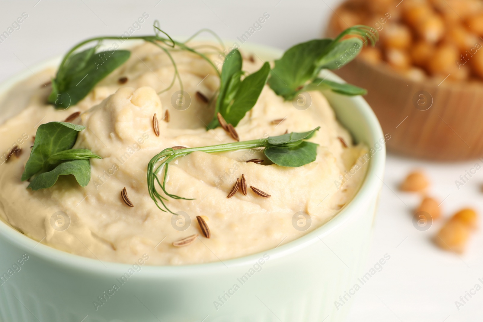 Bowl of tasty hummus with pea leaves on white table, closeup Photo of Bowl of tasty hummus with pea leaves on white table, closeup
