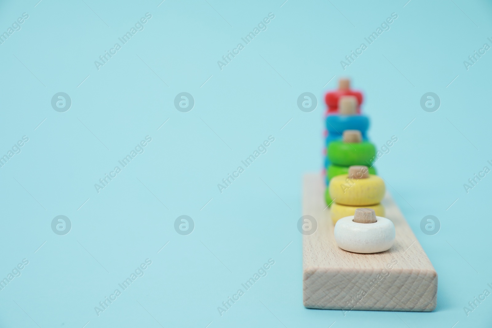 Photo of Stacking and counting game wooden pieces on light blue background, space for text. Educational toy for motor skills development
