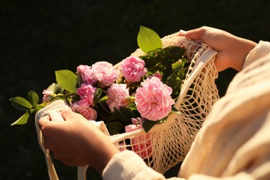Woman holding mesh bag with beautiful tea roses outdoors, closeup