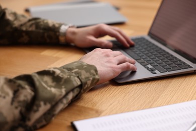 Photo of Military service. Soldier working with laptop at wooden table, closeup