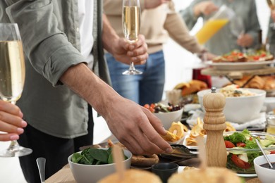 Photo of Man with glass of champagne taking food from buffet indoors, closeup. Brunch table setting