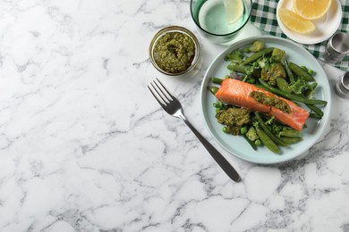 Photo of Tasty cooked salmon with pesto sauce and fresh salad served on white marble table, flat lay. Space for text