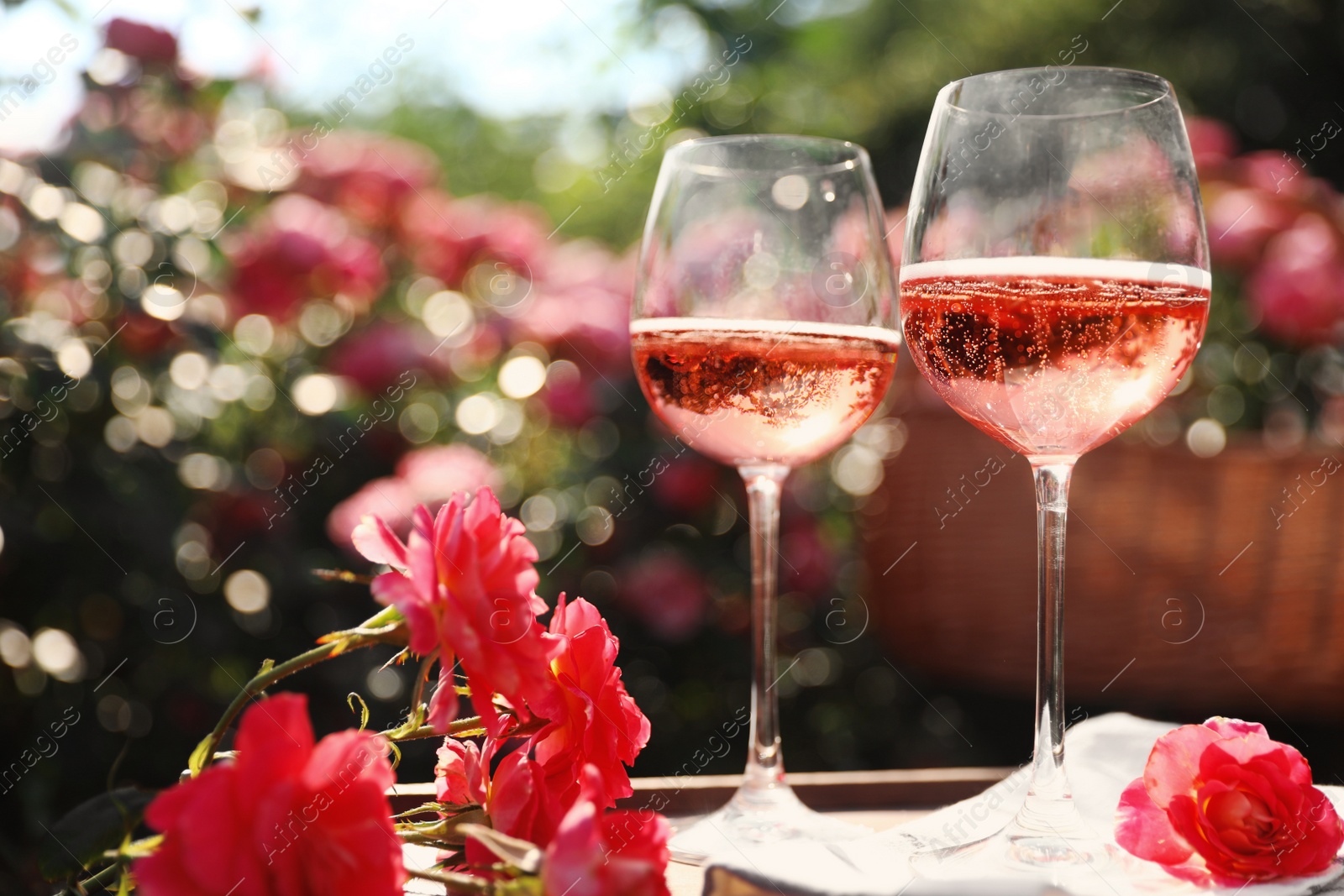 Photo of Glasses of rose wine on table in blooming garden, space for text