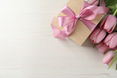 Photo of Beautiful gift box with bow and pink tulip flowers on white wooden background, flat lay. Space for text