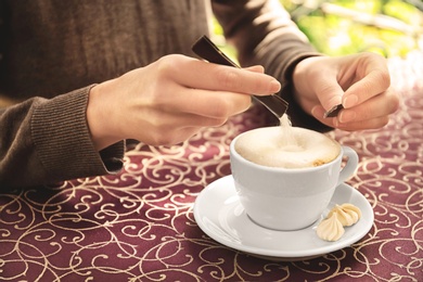 Young woman adding sugar to delicious coffee at table