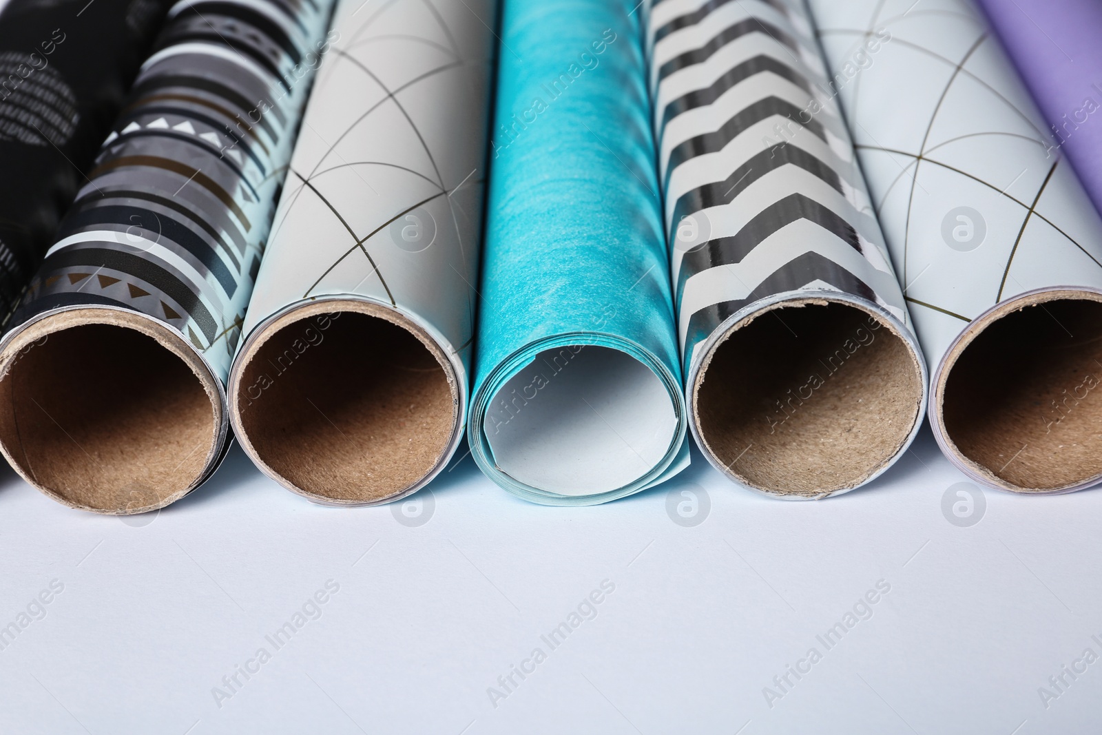 Photo of Rolls of festive wrapping paper on white background, closeup. Gift box packaging ideas