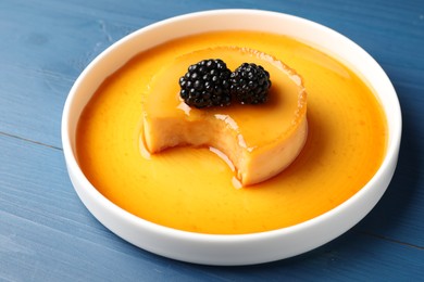 Photo of Delicious pudding with caramel and blackberries on blue wooden table, closeup
