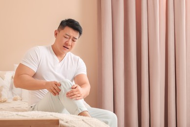 Photo of Asian man suffering from knee pain on bed indoors. Space for text