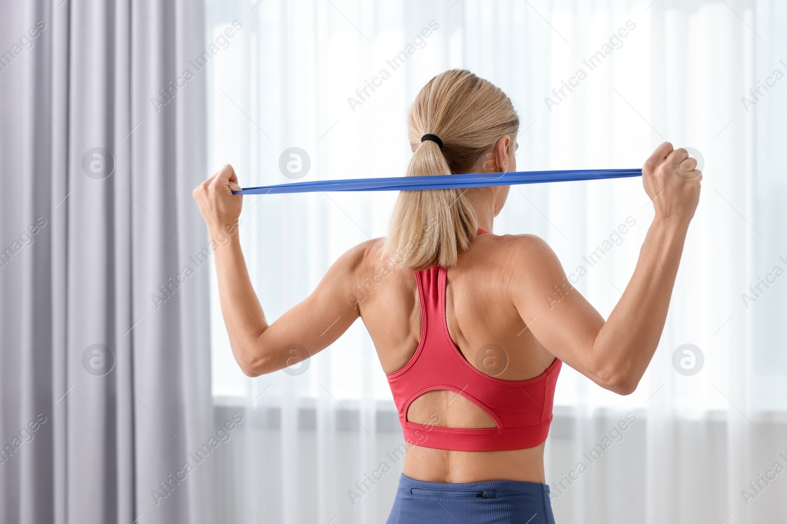 Photo of Fit woman doing exercise with fitness elastic band indoors, back view