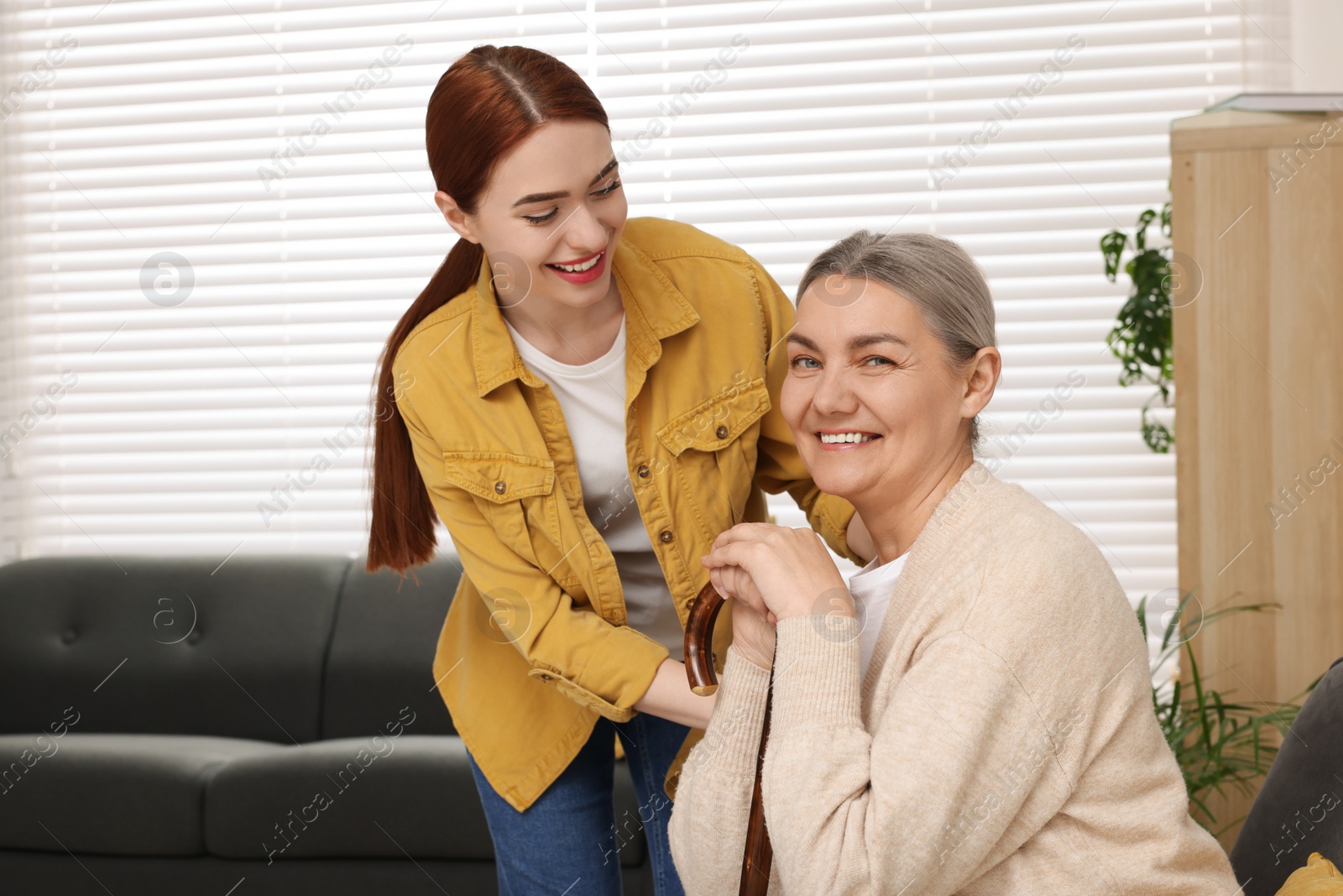 Photo of Caregiver and senior woman with walking cane sitting at home