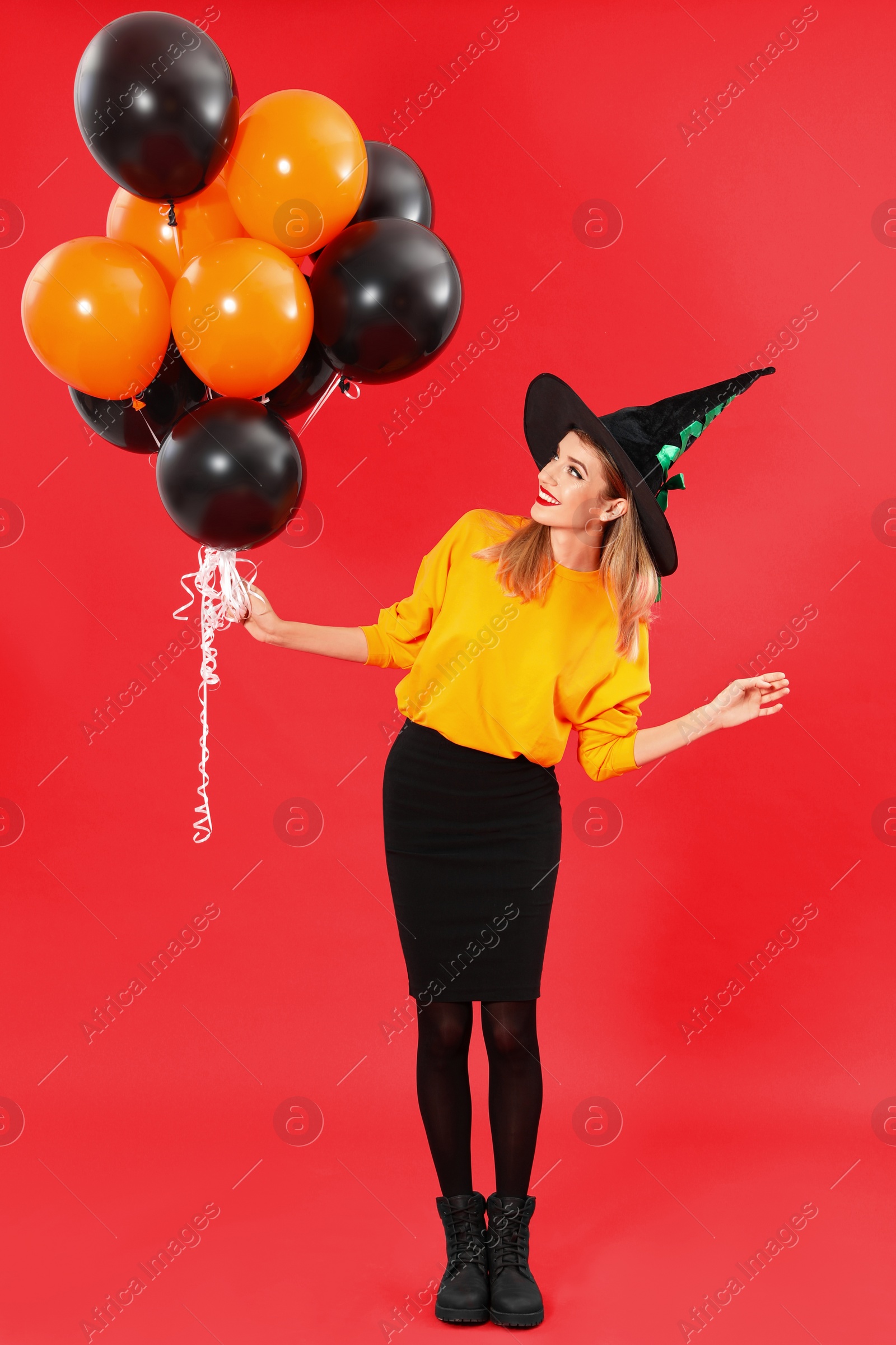 Photo of Beautiful woman wearing witch costume with balloons for Halloween party on red background