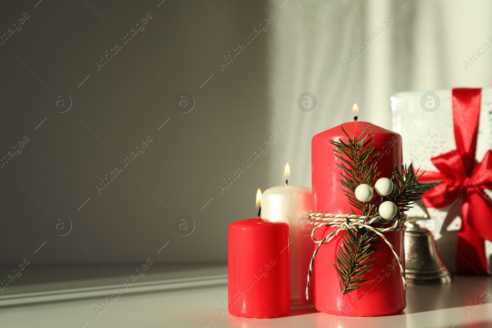 Photo of Burning candles with Christmas decor on white table. Space for text