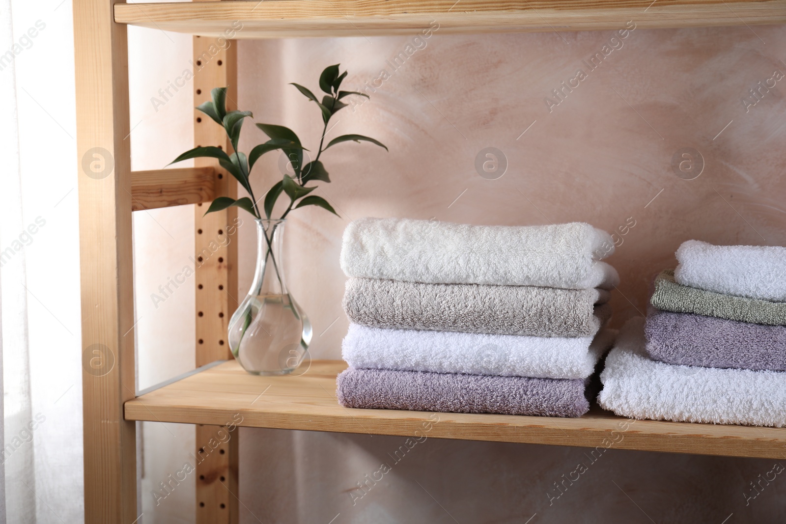 Photo of Stacked soft towels and green leaves on wooden shelf indoors