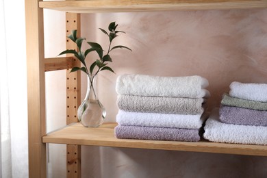 Stacked soft towels and green leaves on wooden shelf indoors