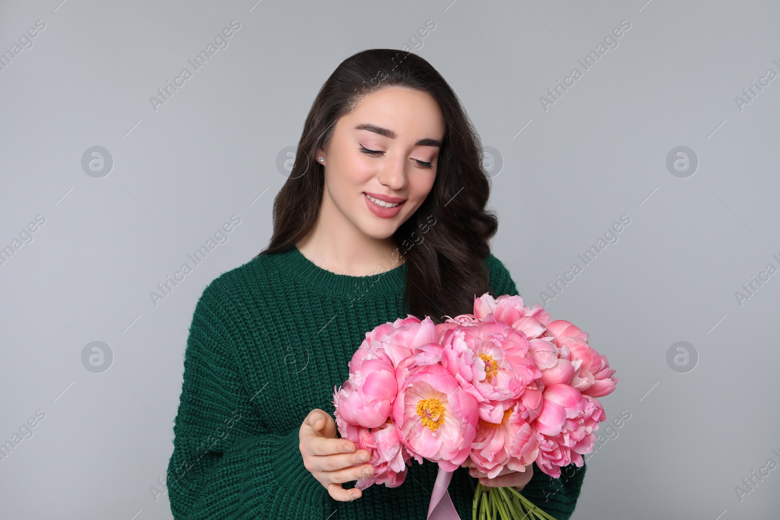 Photo of Beautiful young woman with bouquet of peonies on light grey background