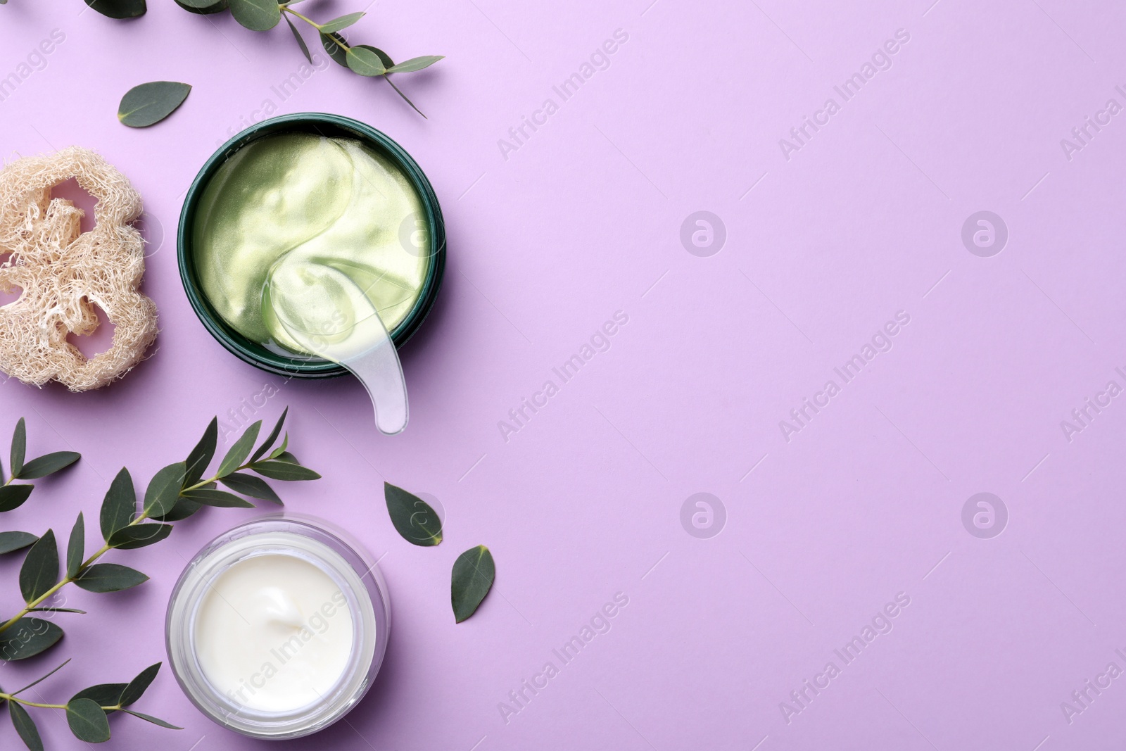 Photo of Package of under eye patches, cream and green twigs on violet background, flat lay with space for text. Cosmetic product