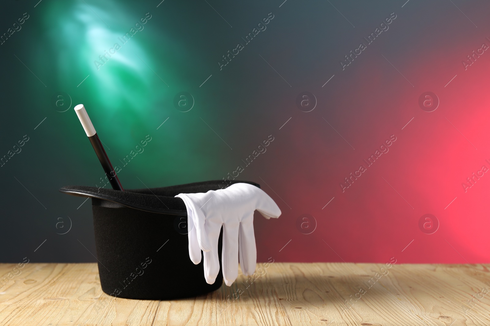 Photo of Magician's hat, wand and gloves on wooden table against color background, space for text