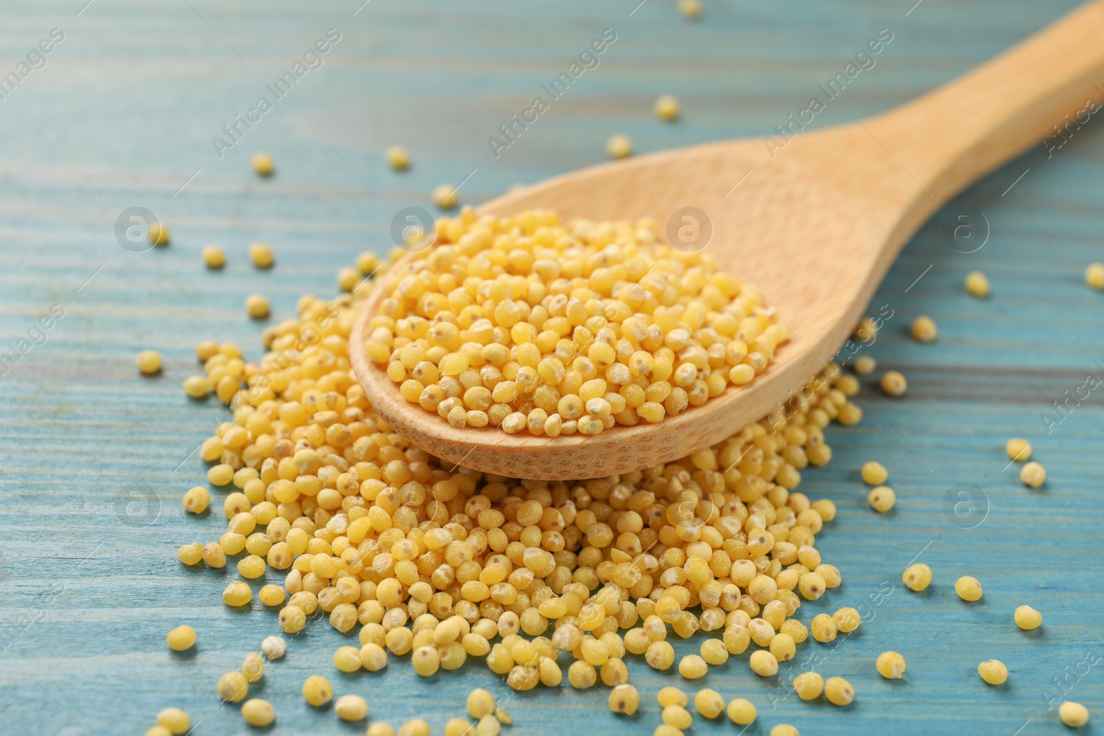 Photo of Spoon with millet groats on blue wooden table, closeup