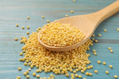 Photo of Spoon with millet groats on blue wooden table, closeup