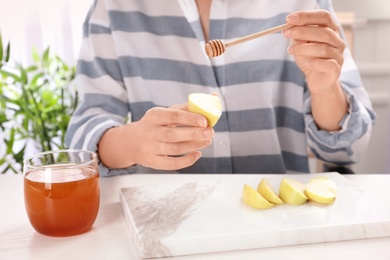 Woman pouring honey onto sliced apple at table