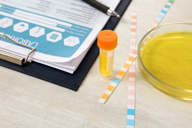 Container with urine sample for analysis, litmus paper and medical report on table in laboratory