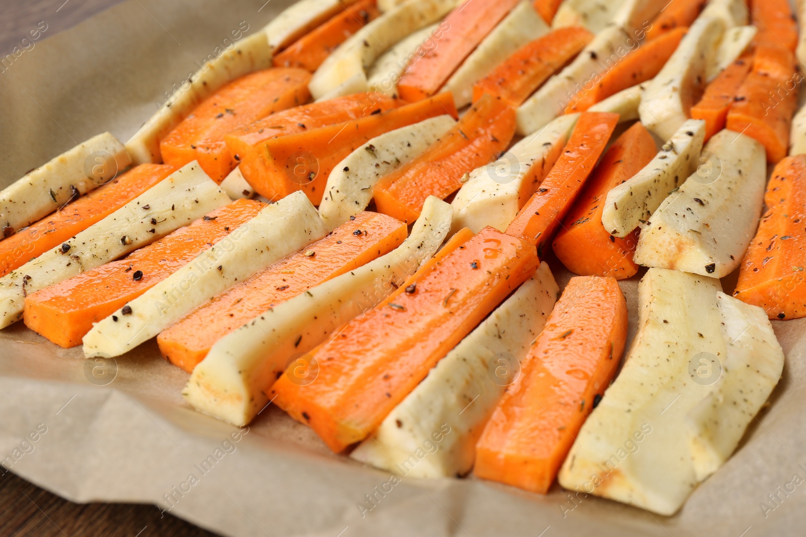 Photo of Baking tray with parchment, parsnips and carrots, closeup