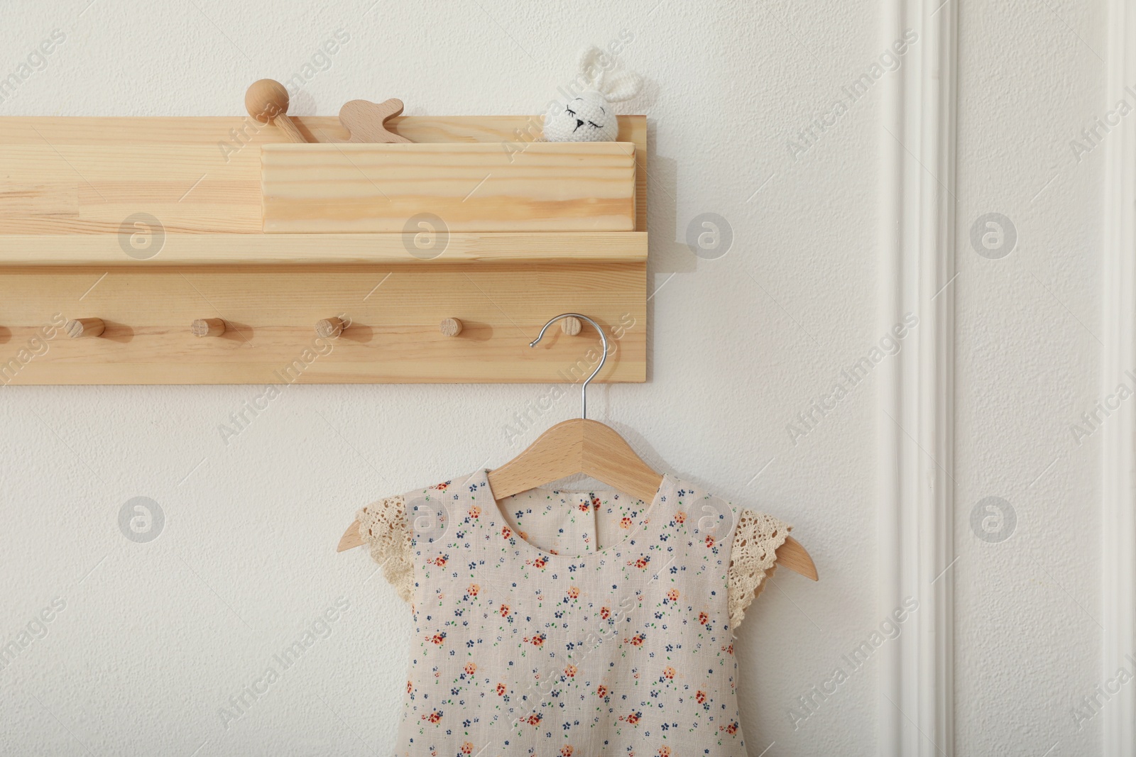 Photo of Wooden rack with cute dress in child room. Interior design