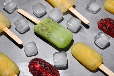 Photo of Delicious pops and ice cubes on grey table. Fruit popsicle