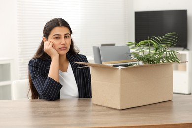 Photo of Unemployment problem. Woman with box of personal belongings at table in office