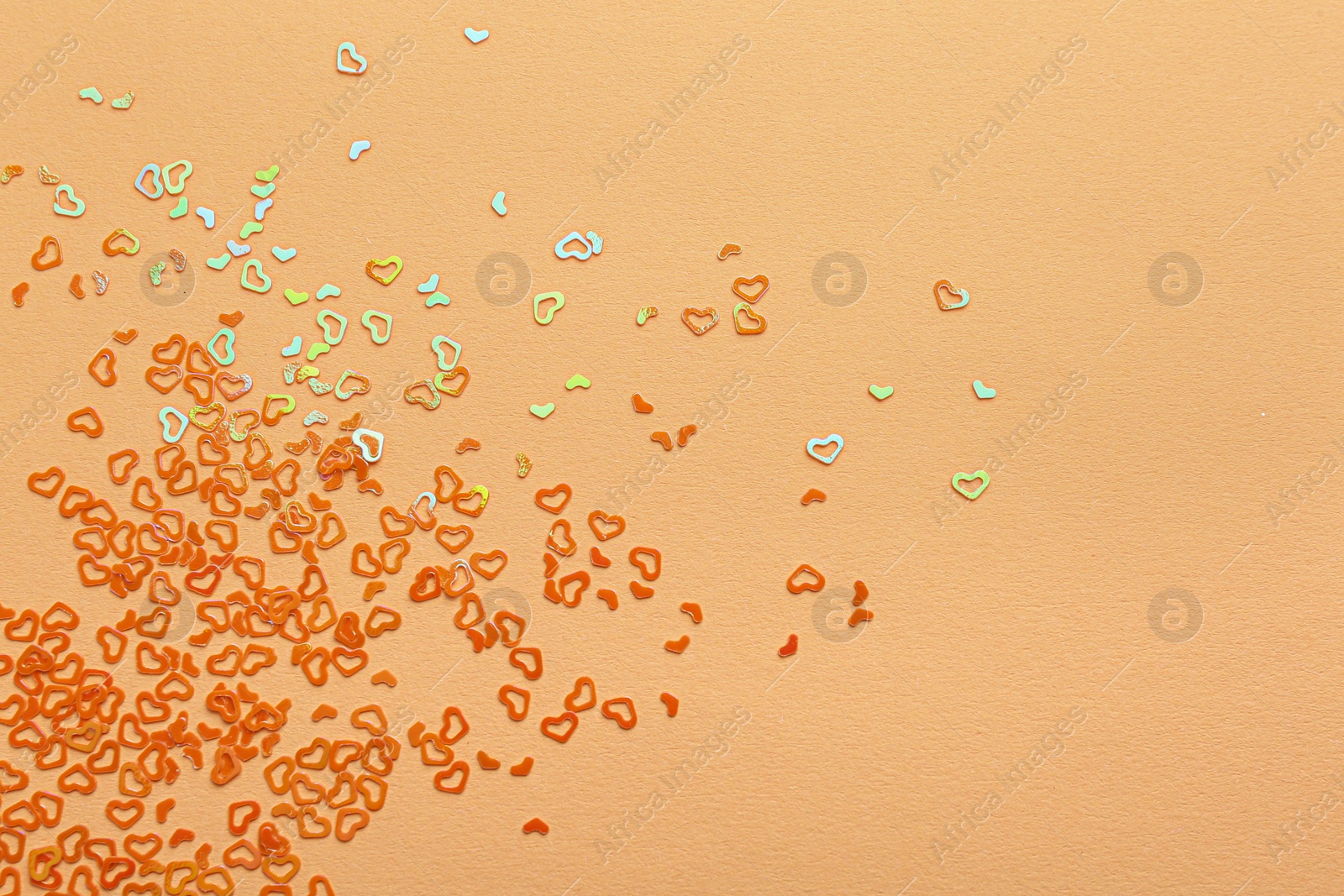 Photo of Shiny bright heart shaped glitter on beige background