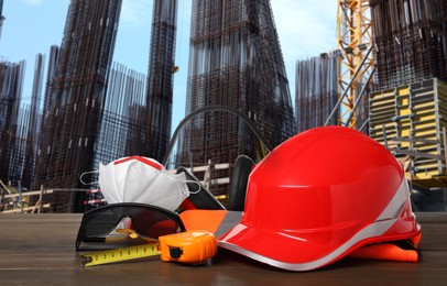 Safety equipment and tools on wooden surface and blurred view of construction site