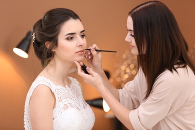 Photo of Professional makeup artist working with young bride in salon