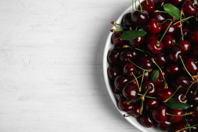 Plate with sweet red cherries on wooden table, top view