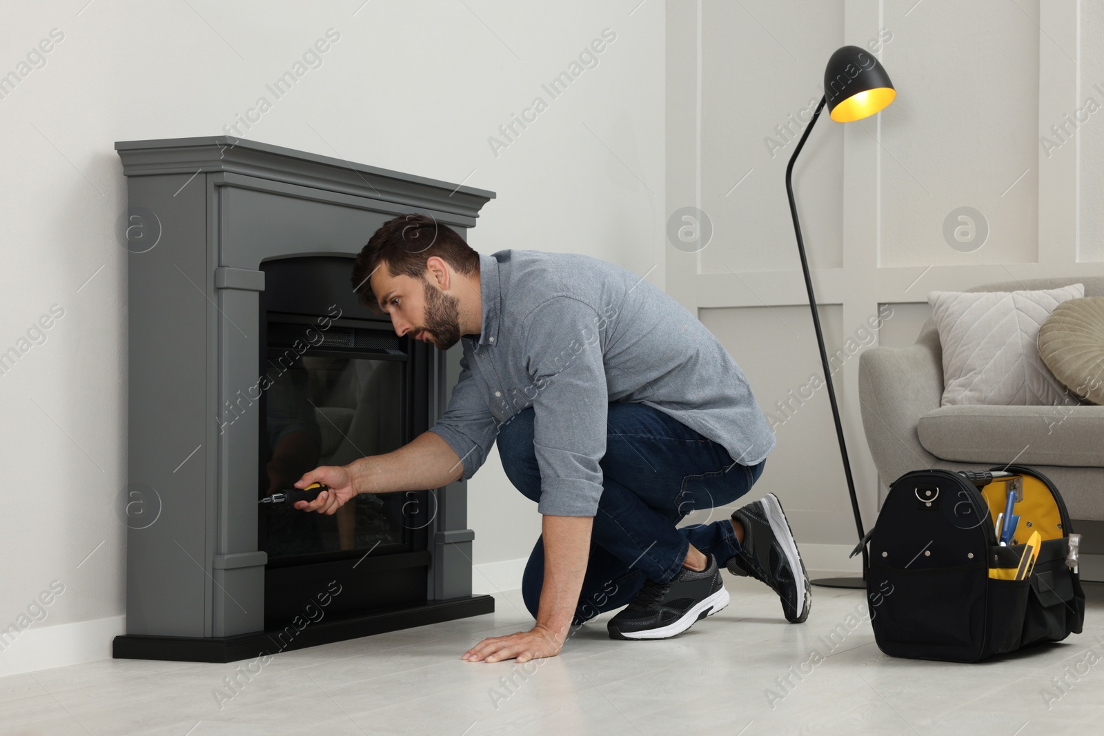 Photo of Man with screwdriver installing electric fireplace near wall in room