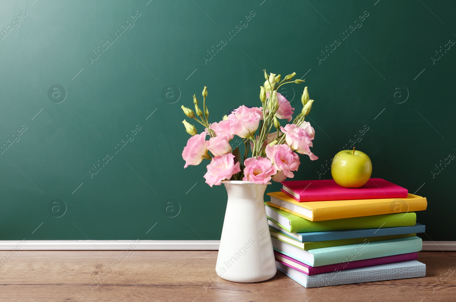 Photo of Vase of flowers, books and apple on wooden table near green chalkboard, space for text. Teacher's day