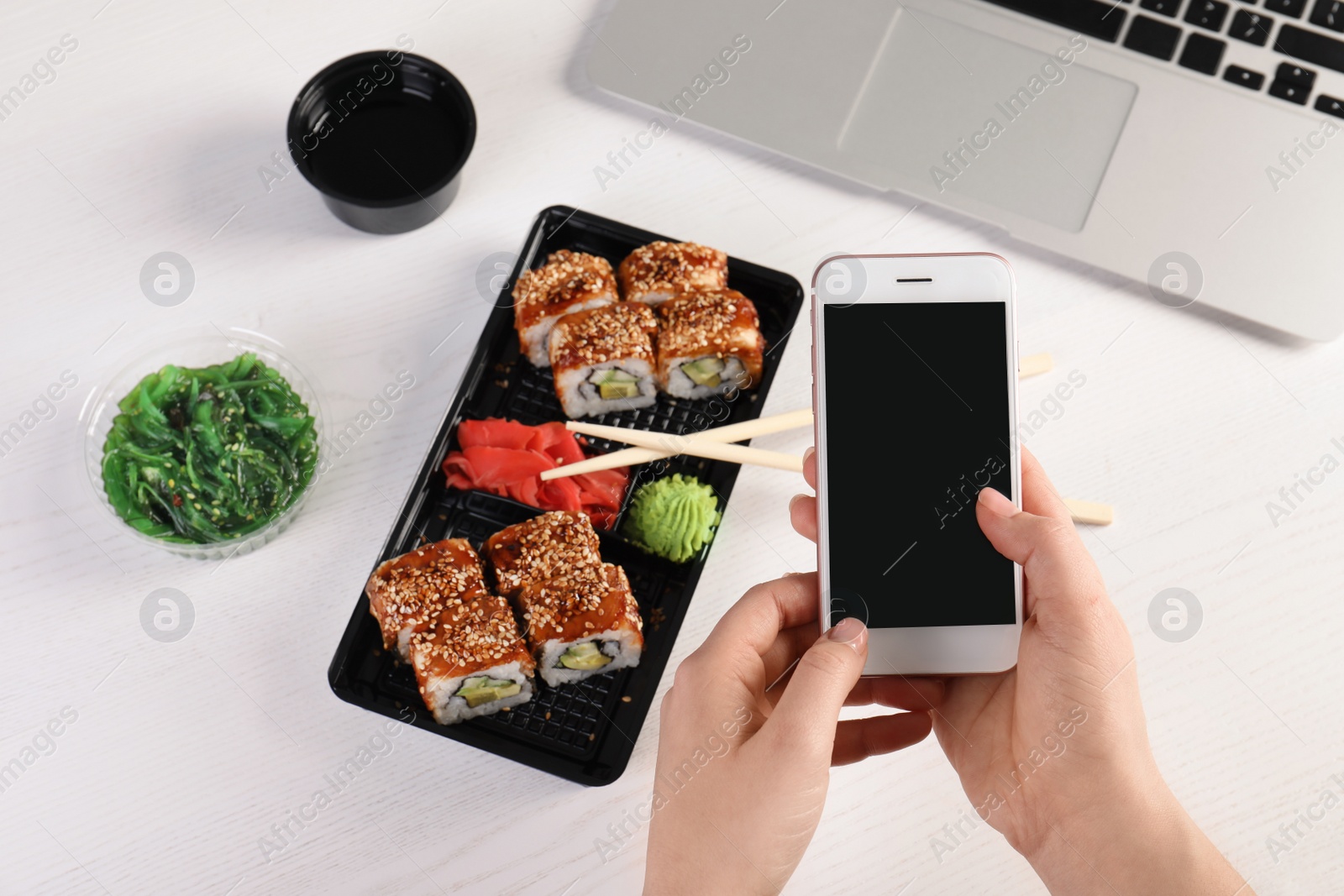 Photo of Woman with mobile phone and sushi rolls at table, space for text. Food delivery