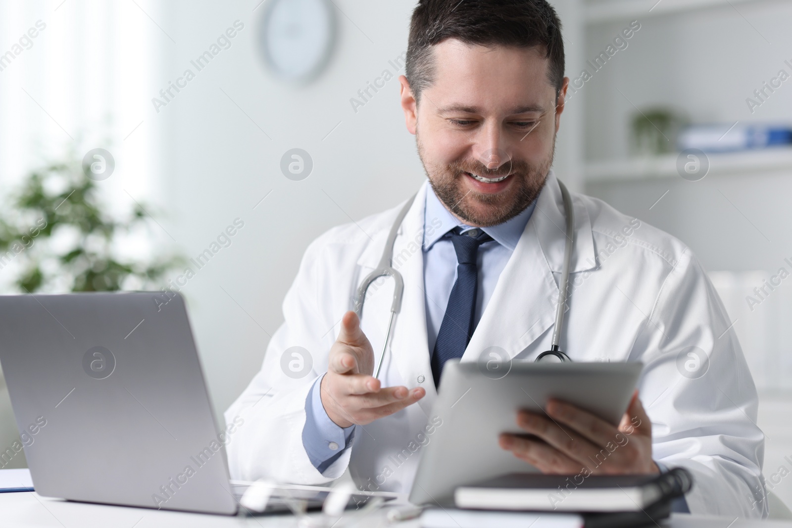 Photo of Smiling doctor having online consultation via tablet at table in clinic
